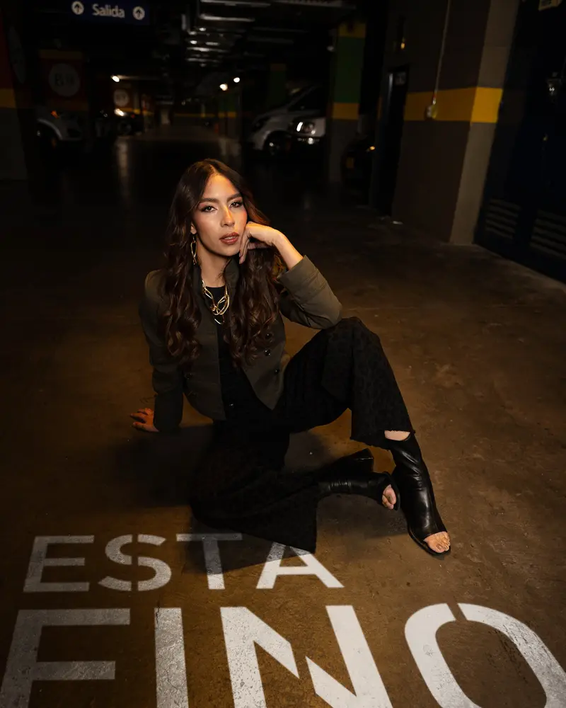 Modelo de la campaña «Está fino» sentada en el piso del parqueadero de VISTO, con «ESTÁ FINO» pintado en el suelo