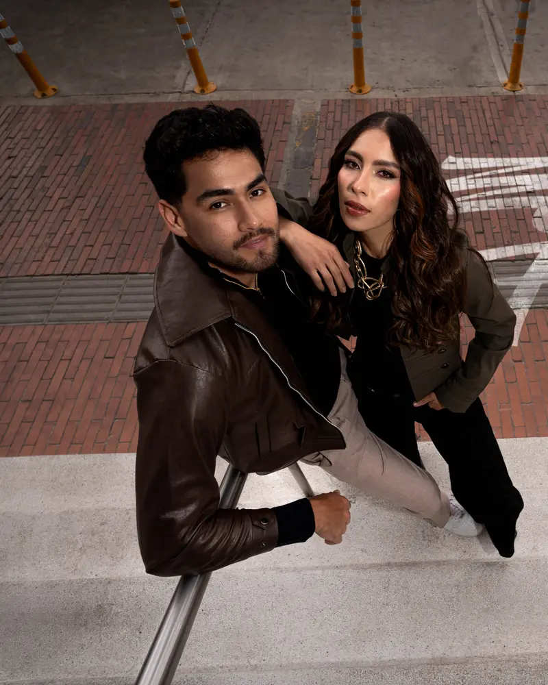 Pareja de la campaña «Está fino» con chaquetas de cuero y verde oliva, fotografiada desde arriba en una escalera