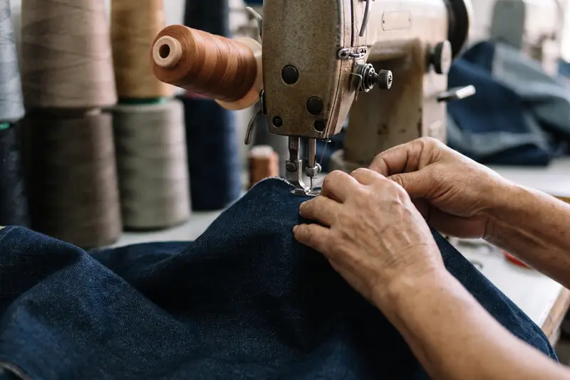 Manos guían el denim bajo la aguja de una máquina de coser industrial