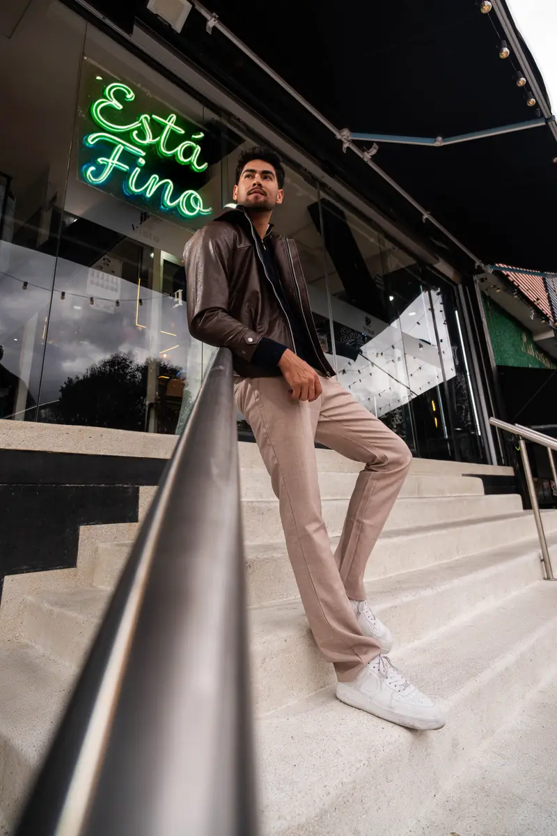 Modelo con chaqueta de cuero café en las escaleras, bajo el neón verde «Está fino»