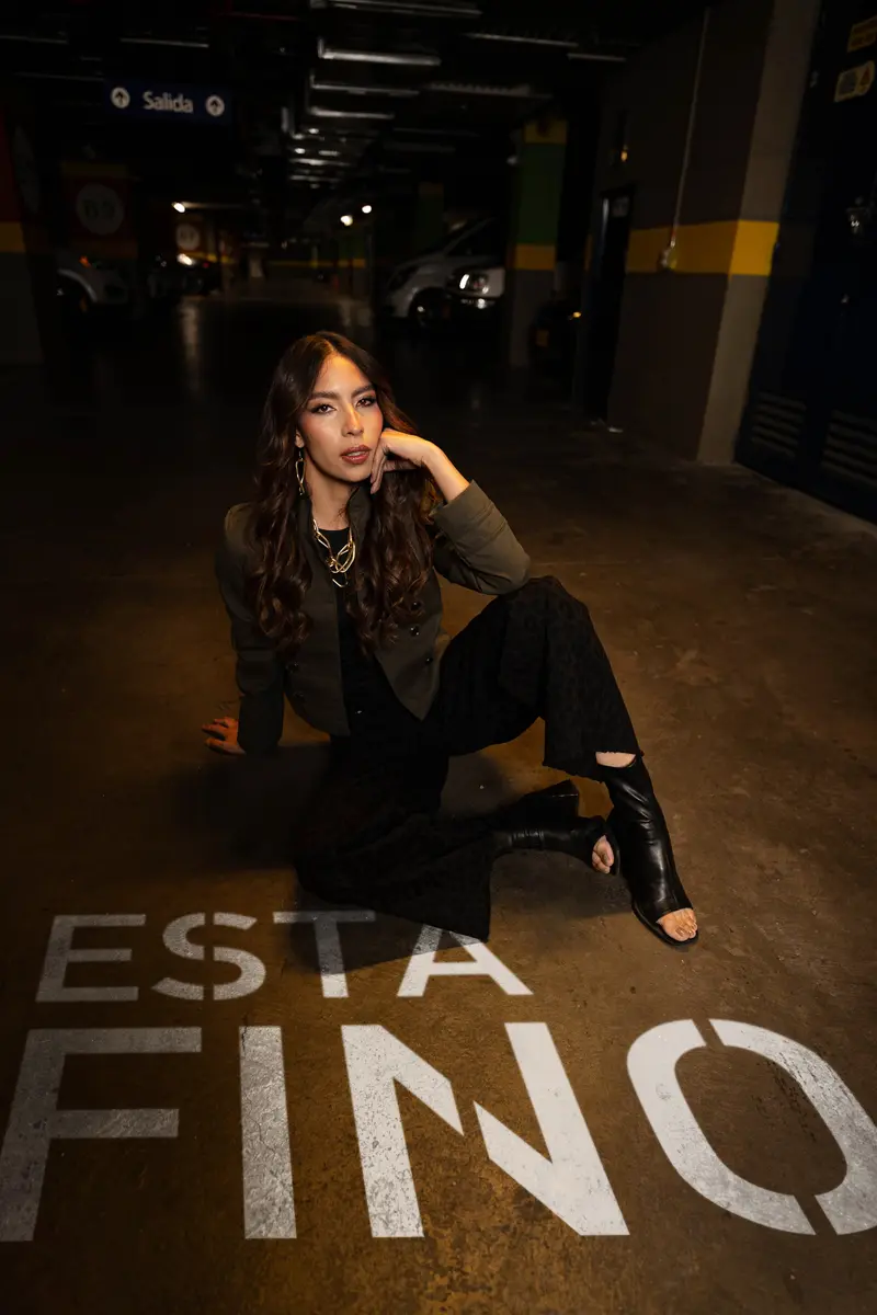 Modelo sentada en el piso de un parqueadero, junto a «ESTÁ FINO» pintado en letras blancas